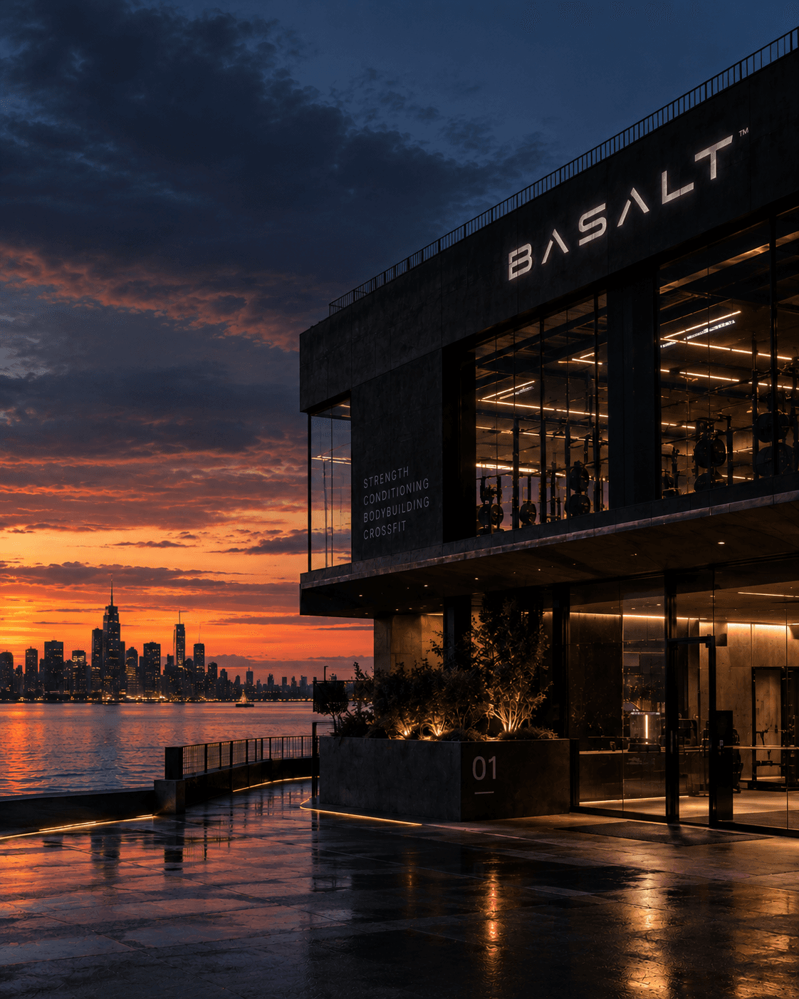 the building exterior at dusk, waterfront behind it, interior lights visible
